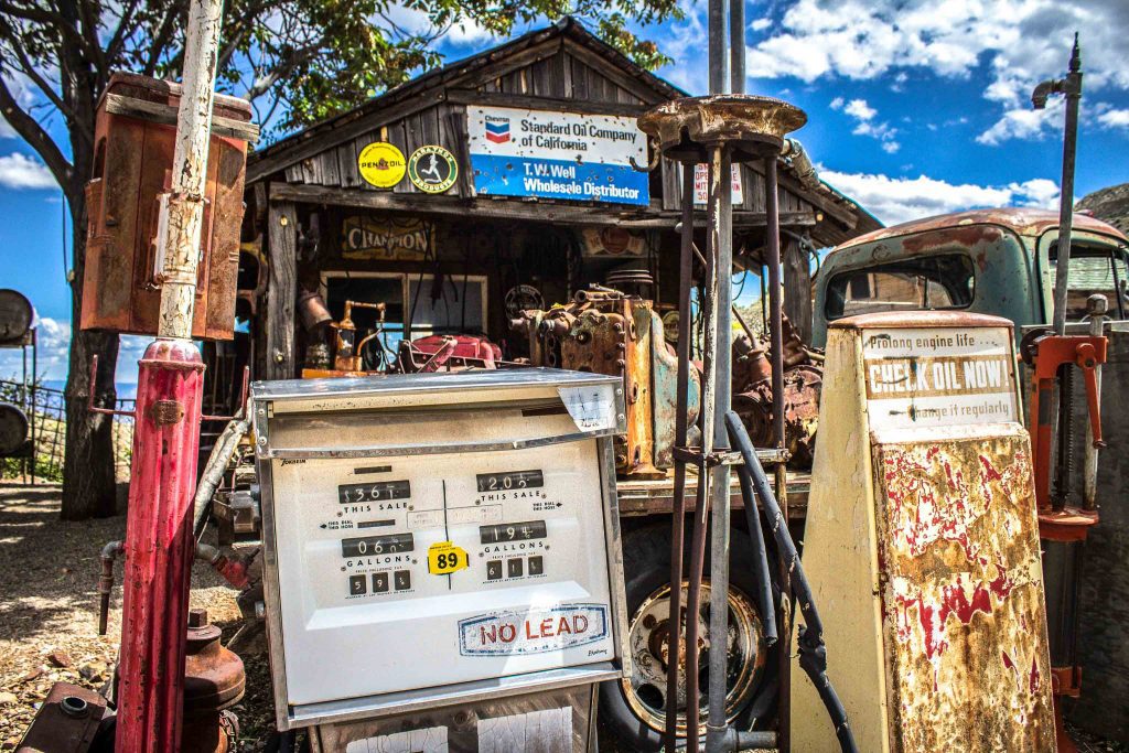 Abandoned gas pumps in front of a wooden building with a sign reading “Standard Oil Company of California. T.W. Well Wholesale Distributor.”