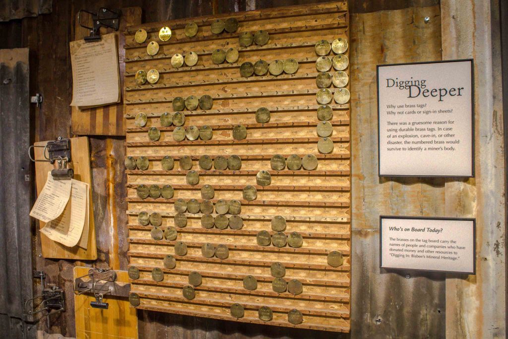 Museum display of a hanging board lined with brown coins, next to a placard titled “Digging Deeper.”