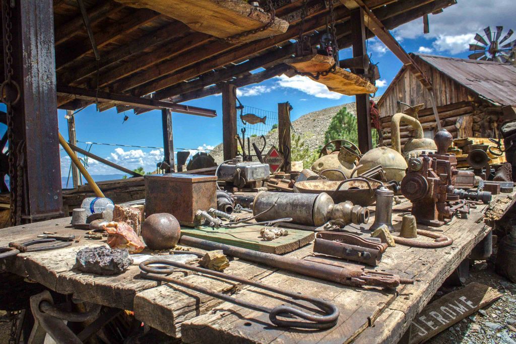 A wooden platform covered in old tools and equipment, in front of a log building and windmill.
