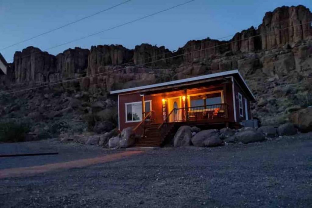 Small bright red cabin with white trim, sitting alone in front of towering sandstone rocks.