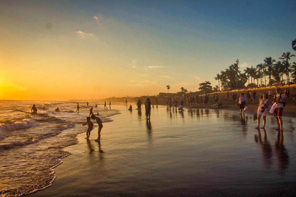 Dozens of tourists wandering around a sandy beach at sunset.