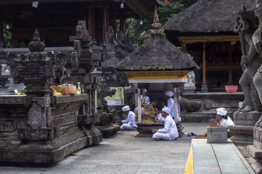 Men in white traditional clothing pray before a stone altar.