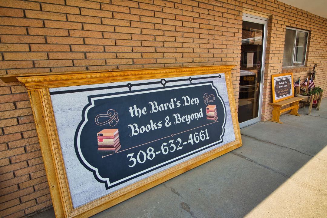 Brick wall with a sign saying "Bard's Den Books and Beyond" along with a phone number.
