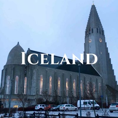 "Iceland" written across a photo of a church with a steeple and clock tower, with cars in the parking lot in front.