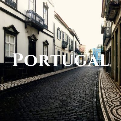 "Portugal" written across a photo of a narrow brick street lined with off-white buildings.