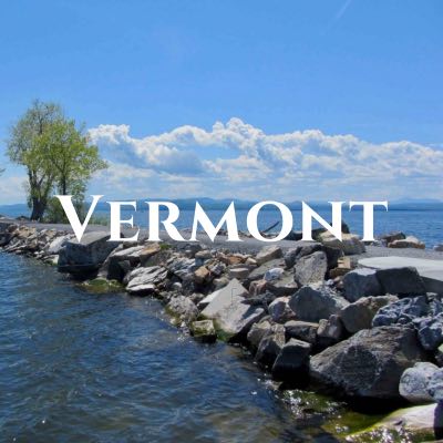 "Vermont" written across a photo of a rocky path stretching across open water.