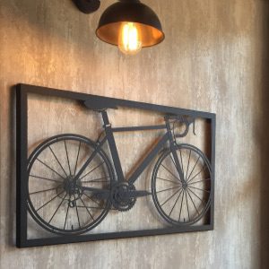 Black metal bicycle inside a metal frame, handing on a wall below a light.