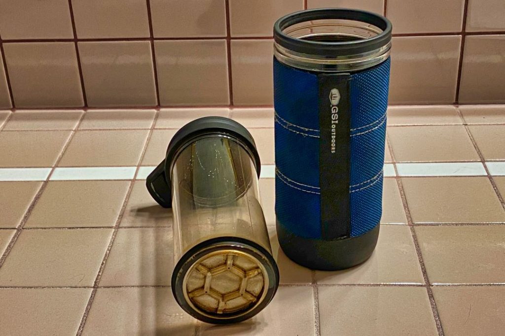Plastic French press plunger on its side next to the base with navy cover.
