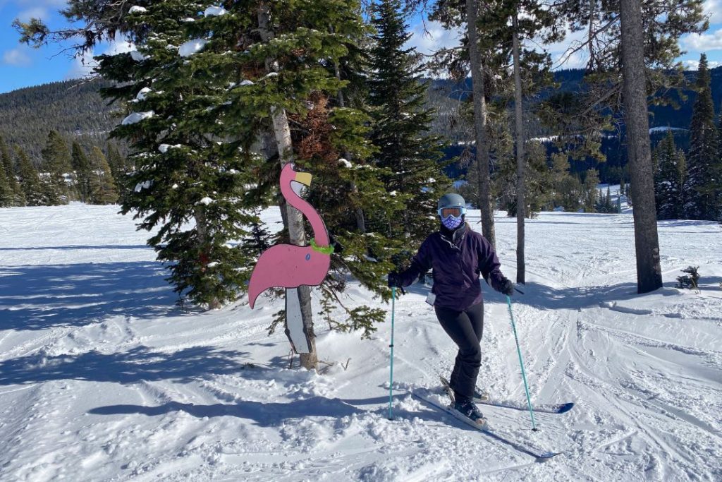 Female skier in dark clothes standing next to a six-foot-tall pink flamingo statue