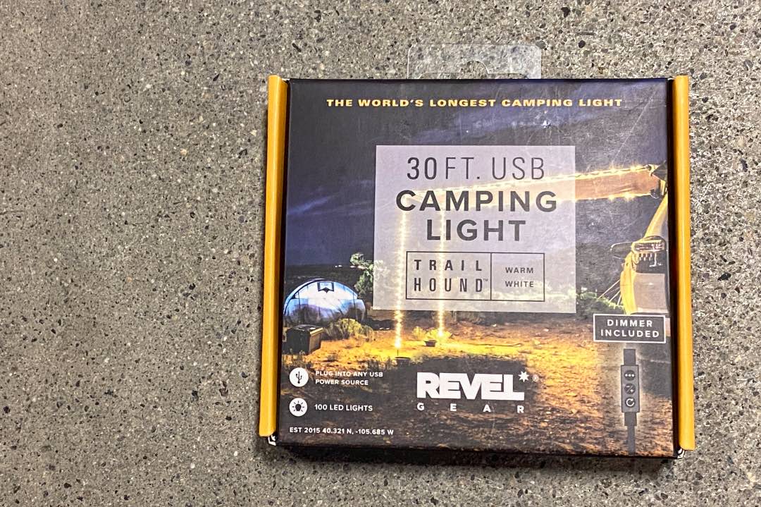 Box with photo of a campground, labeled "30 Ft. USB Camping Light Trail Hound Warm White," and other text reading "The World's Longest Camping Light" and "Revel Gear."