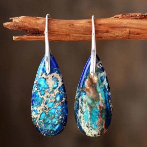 Teardrop blue and copper-colored earrings handing off a wooden branch.