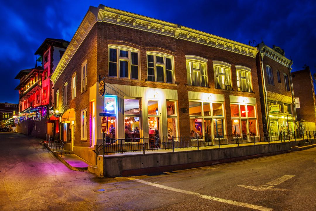 Historic two story building illuminated at night with patrons sitting inside restaurant.
