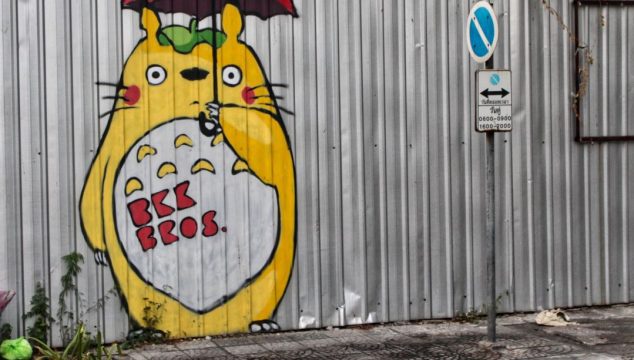 Corrugated metal fence with yellow cat mural painted on it.