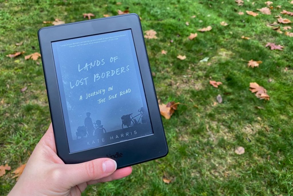 Hand holding a Kindle displaying "Lands of Lost Borders: Out of Bounds on the Silk Road."