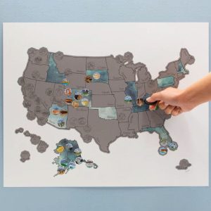 Hand scratching off a blue and silver U.S. map with colorful circles denoting national parks.