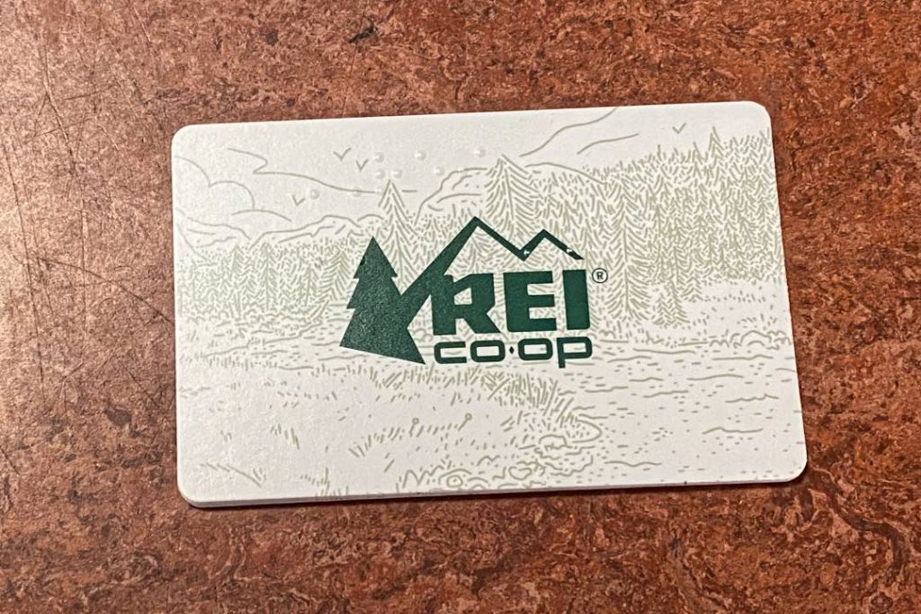 White wallet-sized card with light green forested background and "REI Co-op" written in dark green.