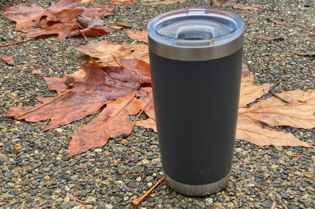 Slate gray thermos with clear plastic top, sitting on leaves and asphalt.