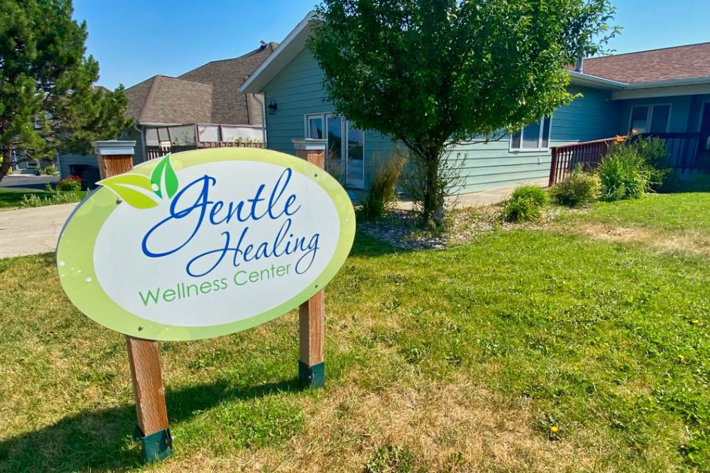 Round sign reading "Gentle Healing Wellness Center" in front of a light green house.