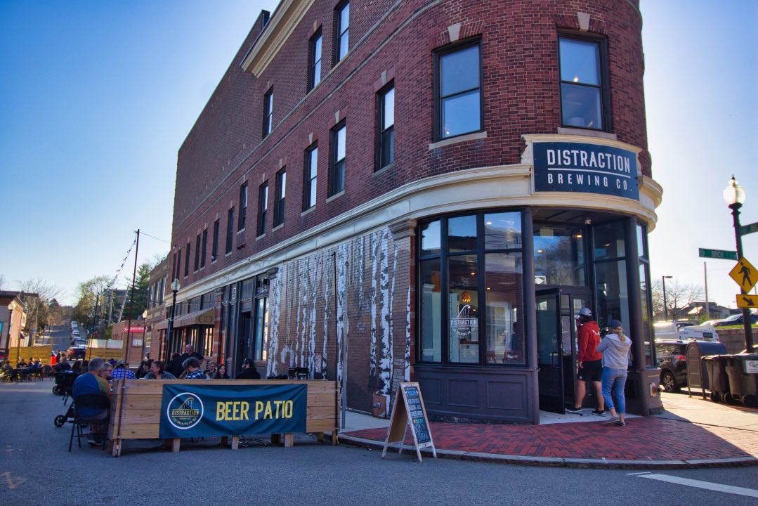 A patio with cafe tables sits behind a banner stating "beer patio" alongside a stately brick building.