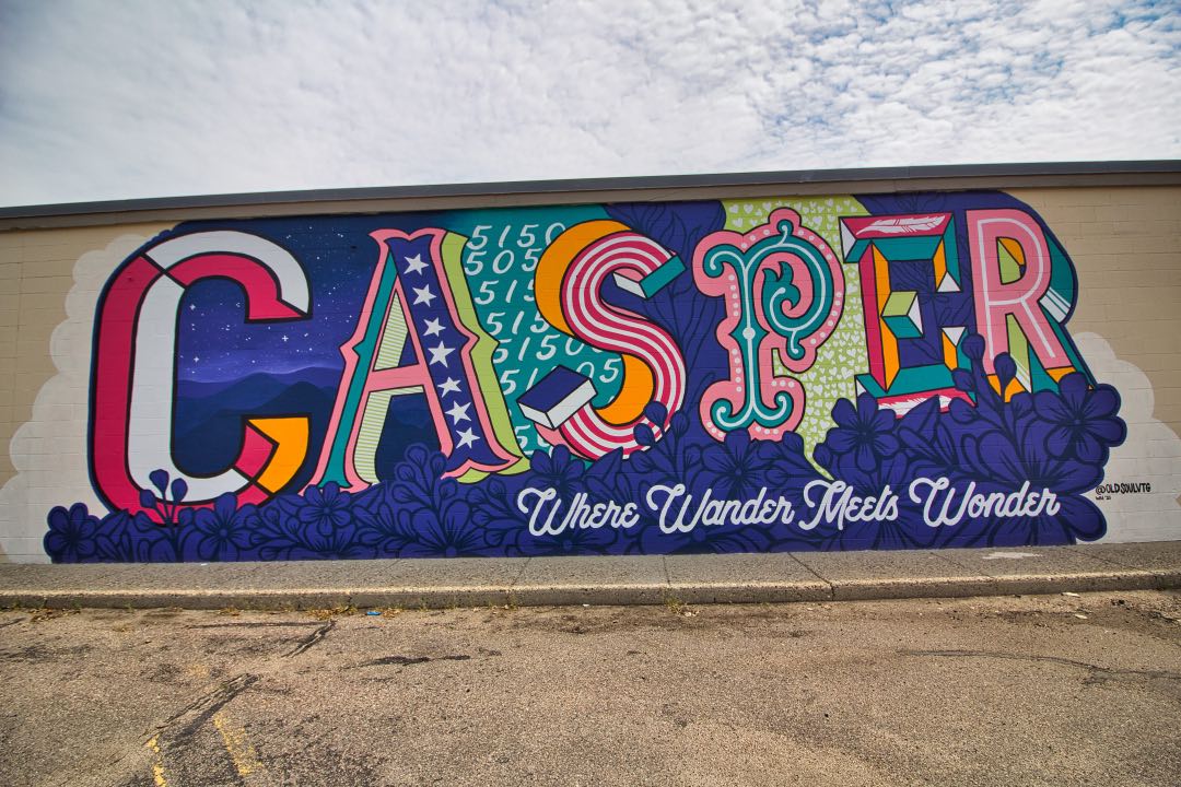 Brick wall covered in pink and blue street art mural that says "Casper, Where Wander Meets Wonder".