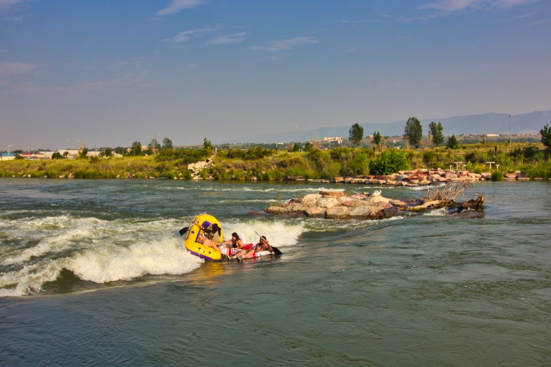 A small yellow raft and two inner tubes floating over a river rapid with the occupants nearly falling out.